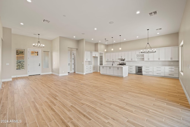 unfurnished living room with beverage cooler, light hardwood / wood-style floors, a high ceiling, and an inviting chandelier