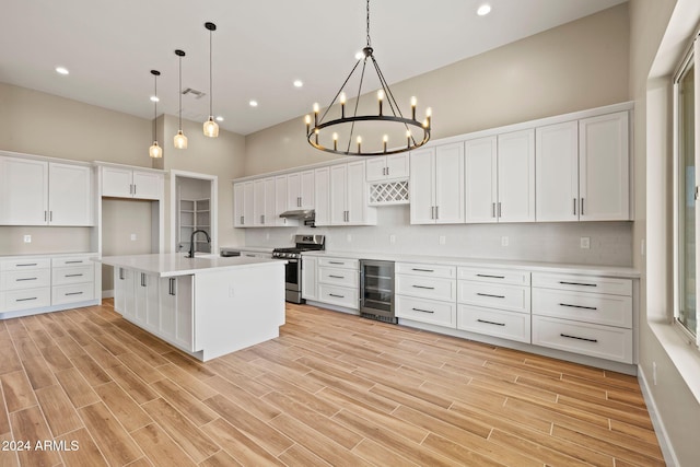 kitchen with pendant lighting, a kitchen island with sink, beverage cooler, and stainless steel range with gas stovetop