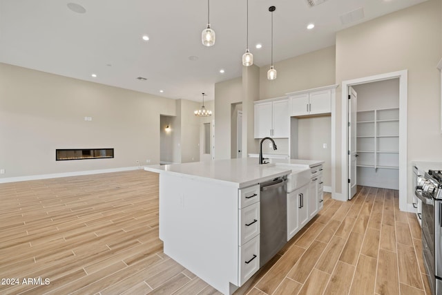 kitchen featuring appliances with stainless steel finishes, sink, a center island with sink, white cabinets, and hanging light fixtures