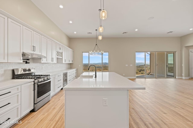 kitchen featuring a kitchen island with sink, sink, white cabinets, stainless steel gas stove, and hanging light fixtures