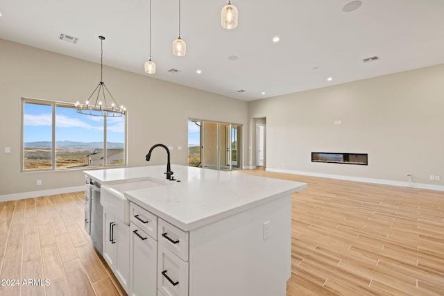 kitchen featuring decorative light fixtures, light stone counters, a kitchen island with sink, and white cabinetry