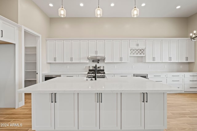 kitchen with appliances with stainless steel finishes, light stone counters, pendant lighting, a center island with sink, and white cabinetry