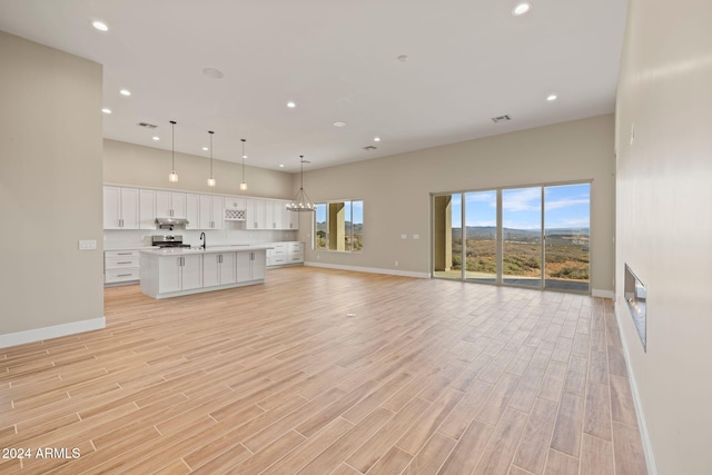 unfurnished living room featuring light hardwood / wood-style floors, a towering ceiling, and sink