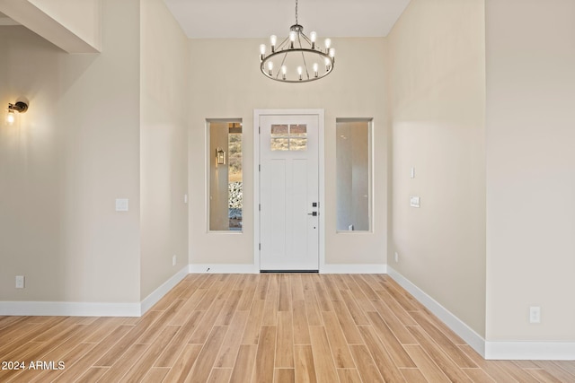 foyer entrance featuring a towering ceiling, a chandelier, and light hardwood / wood-style floors