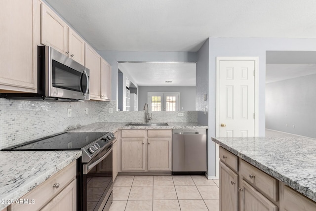 kitchen with light tile patterned floors, light stone counters, a sink, appliances with stainless steel finishes, and decorative backsplash