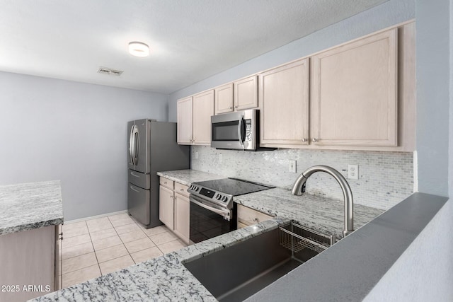 kitchen with light tile patterned flooring, a sink, appliances with stainless steel finishes, light brown cabinetry, and tasteful backsplash