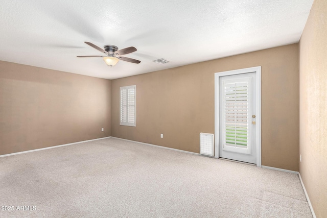 empty room featuring a textured ceiling, ceiling fan, carpet floors, visible vents, and baseboards