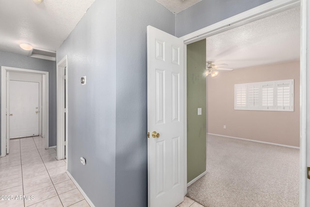 corridor featuring light tile patterned floors, baseboards, and a textured ceiling