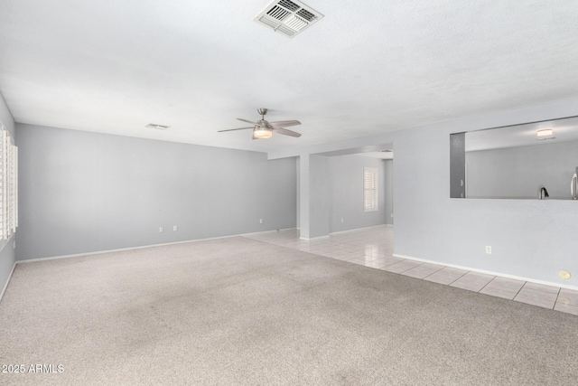 tiled empty room featuring carpet floors, visible vents, baseboards, and a ceiling fan