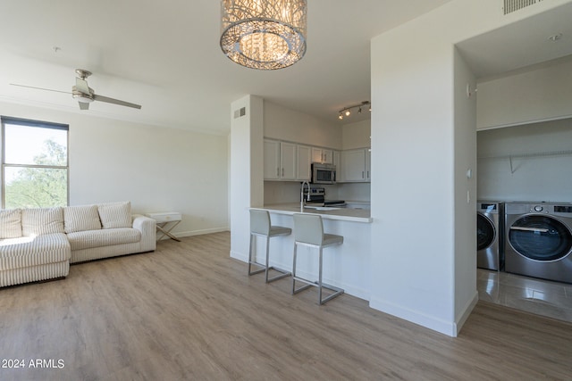 kitchen featuring white cabinets, a kitchen bar, separate washer and dryer, light hardwood / wood-style floors, and stainless steel appliances