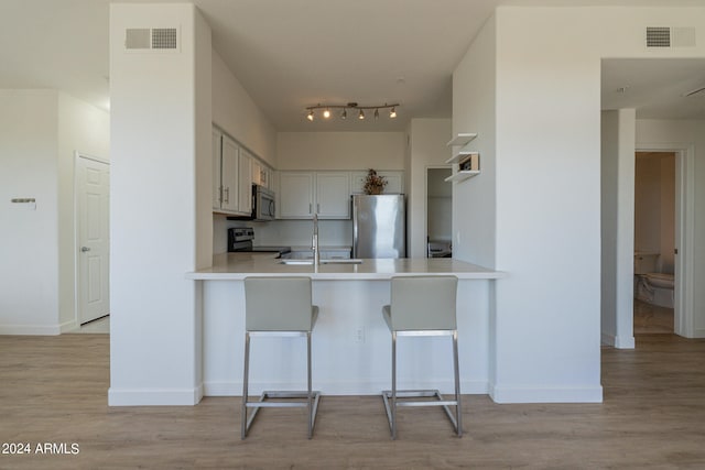 kitchen with kitchen peninsula, a breakfast bar, light hardwood / wood-style flooring, sink, and stainless steel appliances