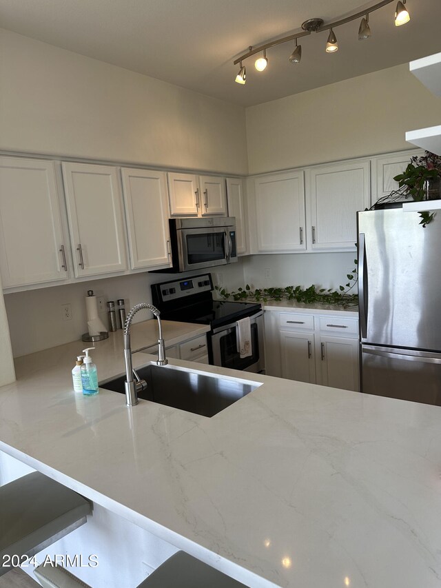 kitchen with white cabinets, stainless steel appliances, sink, and light stone counters