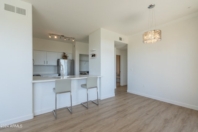 kitchen featuring light wood-type flooring, kitchen peninsula, white cabinets, stainless steel refrigerator, and a breakfast bar area