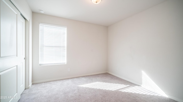 spare room with baseboards and light colored carpet