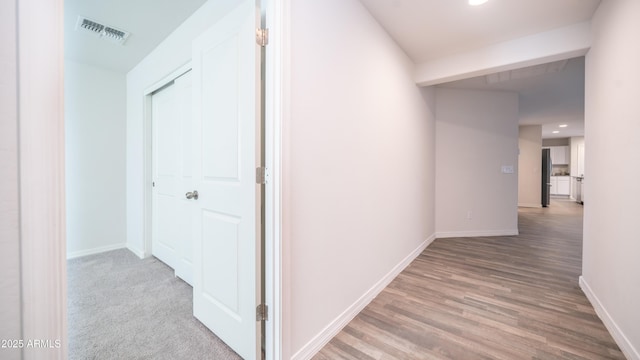 hall featuring light wood-style floors, baseboards, and visible vents