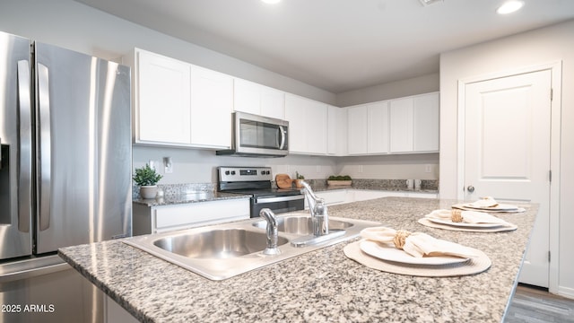 kitchen featuring stainless steel appliances, a sink, white cabinets, light stone countertops, and an island with sink