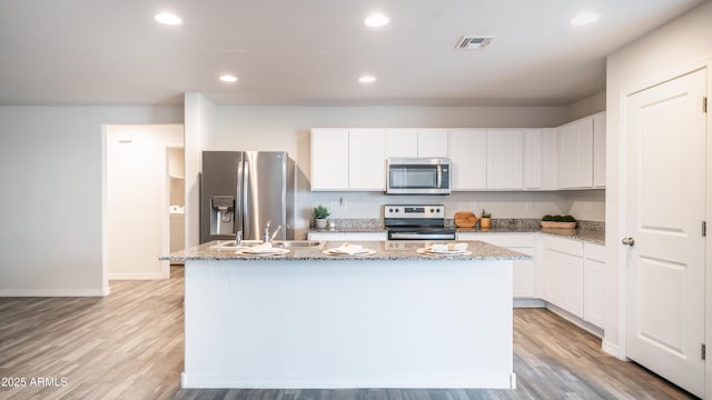 kitchen with stainless steel appliances, a sink, a center island with sink, and white cabinets