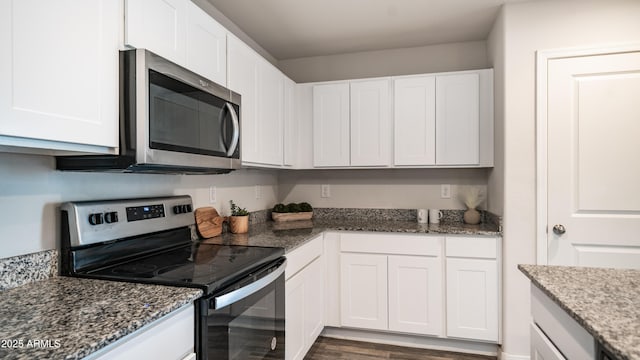 kitchen featuring dark wood finished floors, appliances with stainless steel finishes, white cabinets, and dark stone countertops