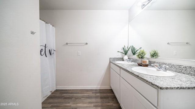 bathroom with double vanity, baseboards, a sink, and wood finished floors