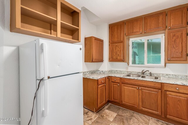 kitchen featuring light tile patterned floors, white fridge, light stone countertops, and sink