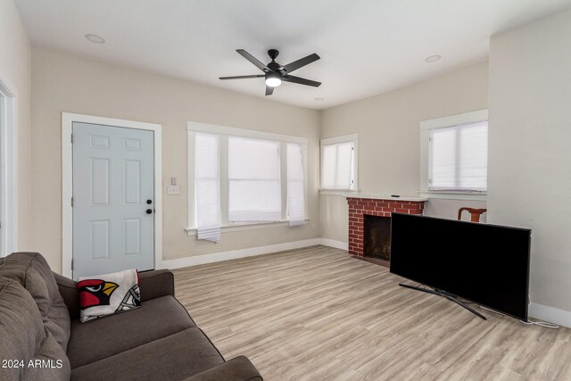 living room with ceiling fan, light hardwood / wood-style flooring, and a brick fireplace