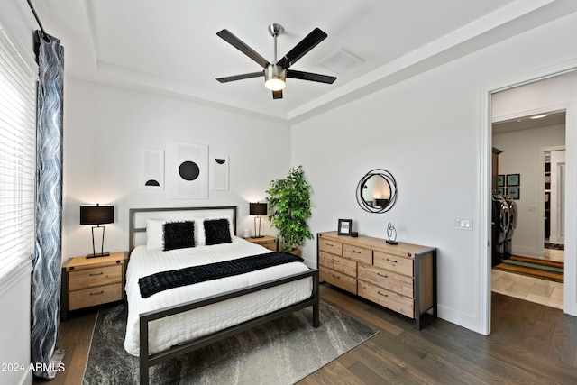 bedroom with washing machine and clothes dryer, a raised ceiling, ceiling fan, and dark wood-type flooring