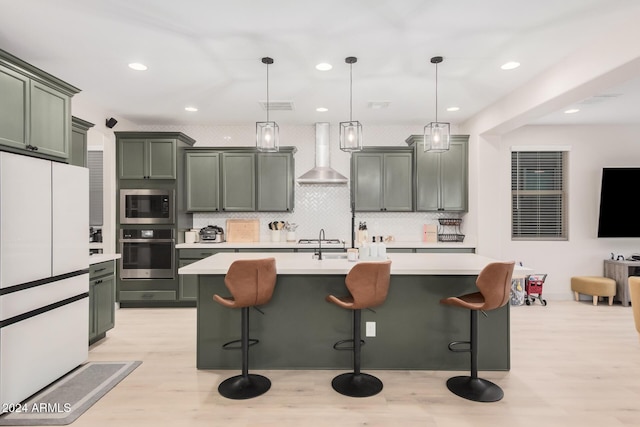 kitchen with pendant lighting, stainless steel appliances, a center island with sink, and wall chimney range hood