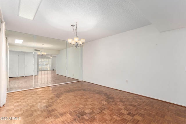 empty room featuring baseboards, a textured ceiling, visible vents, and a notable chandelier