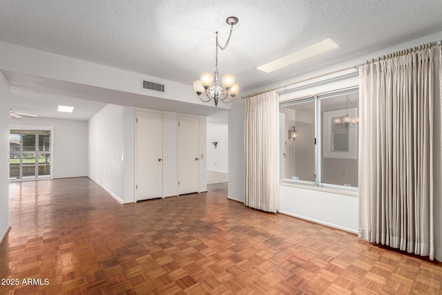 unfurnished room with visible vents, a textured ceiling, baseboards, and ceiling fan with notable chandelier