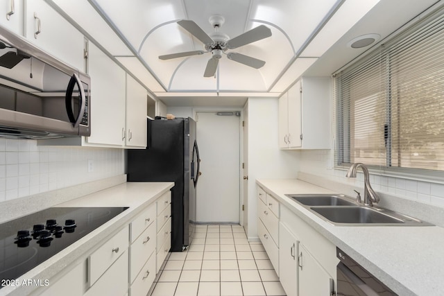 kitchen featuring light tile patterned floors, decorative backsplash, white cabinets, black appliances, and a sink