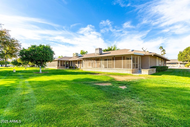 rear view of property featuring a sunroom, a chimney, a lawn, and stucco siding