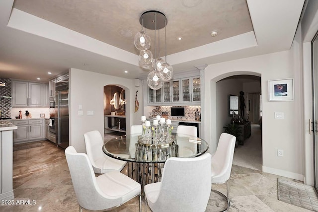 dining area with a raised ceiling, recessed lighting, arched walkways, and baseboards