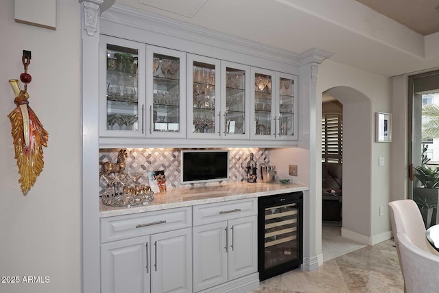 bar with beverage cooler, backsplash, arched walkways, baseboards, and a dry bar