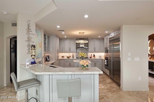 kitchen featuring gray cabinetry, appliances with stainless steel finishes, a peninsula, arched walkways, and a sink