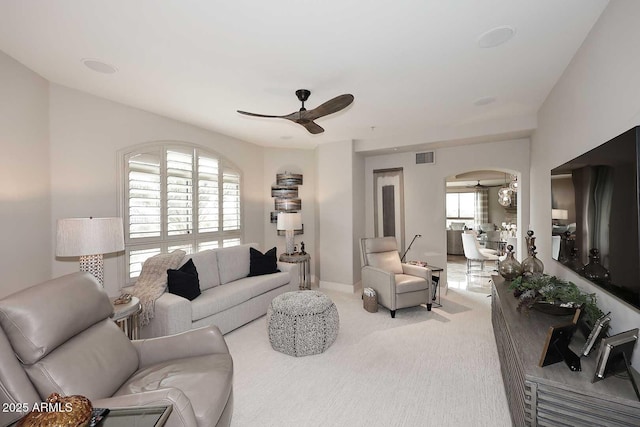 carpeted living area with a wealth of natural light, visible vents, arched walkways, and a ceiling fan