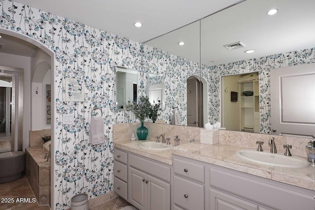 full bath featuring a sink, visible vents, double vanity, and wallpapered walls