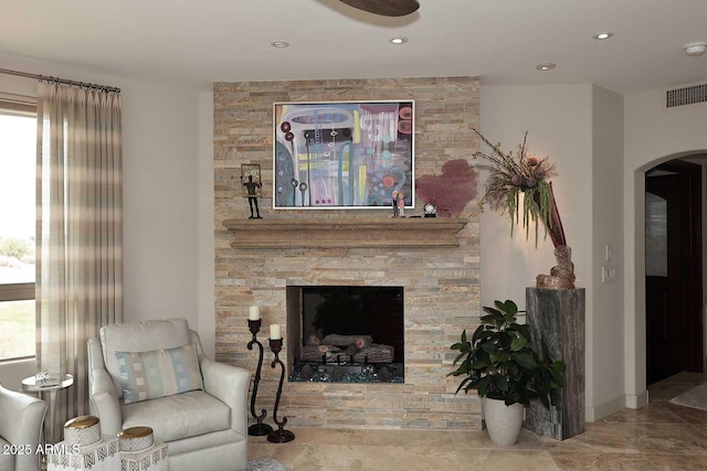 living room with arched walkways, visible vents, recessed lighting, and a stone fireplace