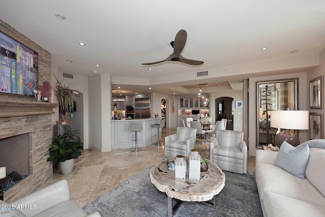 living room with visible vents, a stone fireplace, recessed lighting, arched walkways, and a ceiling fan