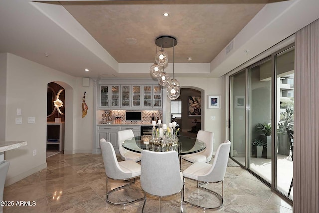 dining area with a tray ceiling, arched walkways, marble finish floor, and visible vents