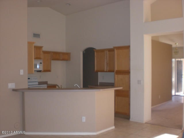 1412 E Oakland St, Gilbert, AZ 85295 - kitchen featuring white microwave, high vaulted ceiling, range, light tile patterned flooring, and a peninsula