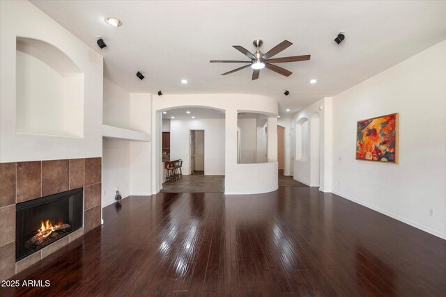 43998 W Palo Abeto Dr, Maricopa, AZ 85138 - unfurnished living room with dark wood-style flooring, arched walkways, ceiling fan, and a tiled fireplace