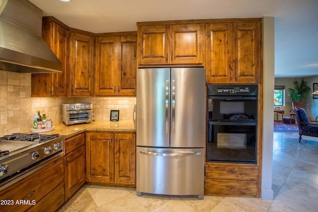 kitchen featuring wall chimney range hood, stainless steel fridge, stovetop, double oven, and light stone counters