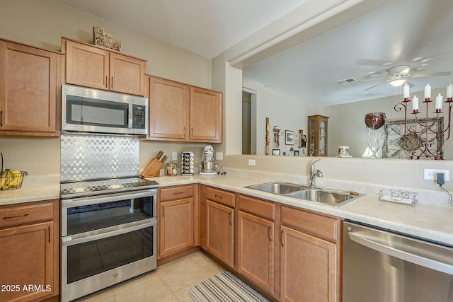 kitchen with kitchen peninsula, stainless steel appliances, ceiling fan, sink, and light tile patterned flooring