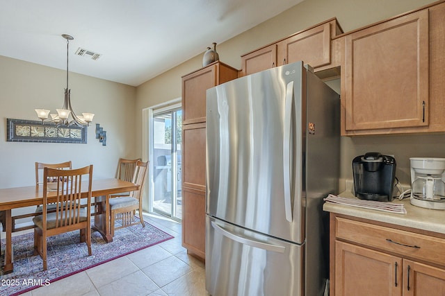 kitchen with stainless steel fridge, light tile patterned floors, light brown cabinets, decorative light fixtures, and an inviting chandelier