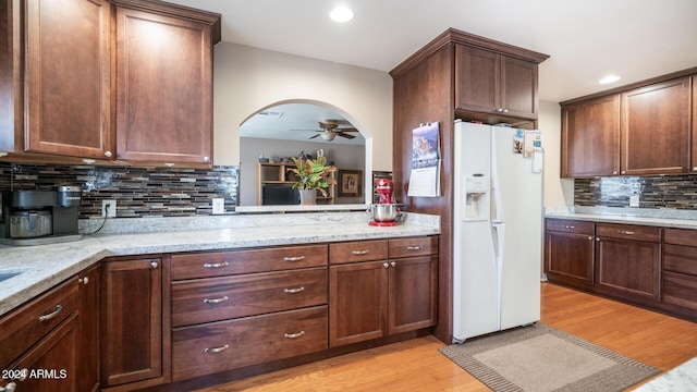 kitchen with backsplash, light hardwood / wood-style flooring, ceiling fan, light stone countertops, and white fridge with ice dispenser