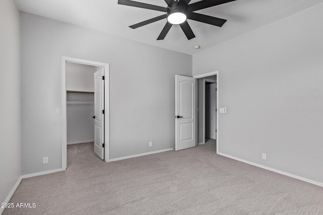 unfurnished bedroom featuring a walk in closet, carpet floors, baseboards, and ceiling fan