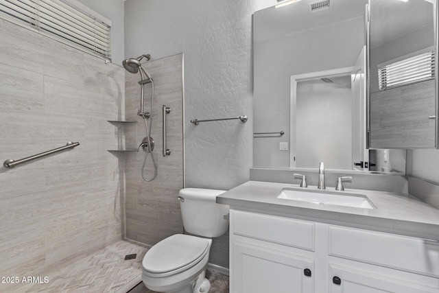 bathroom featuring vanity, a textured wall, a tile shower, toilet, and visible vents