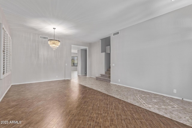 unfurnished living room with wood finished floors, visible vents, baseboards, a chandelier, and stairs