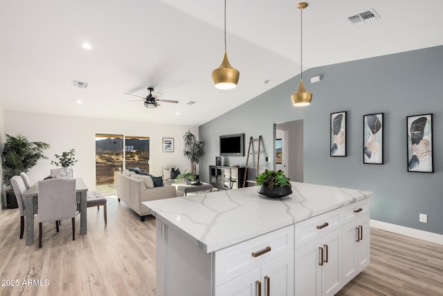 kitchen featuring lofted ceiling, light hardwood / wood-style flooring, light stone counters, white cabinets, and decorative light fixtures