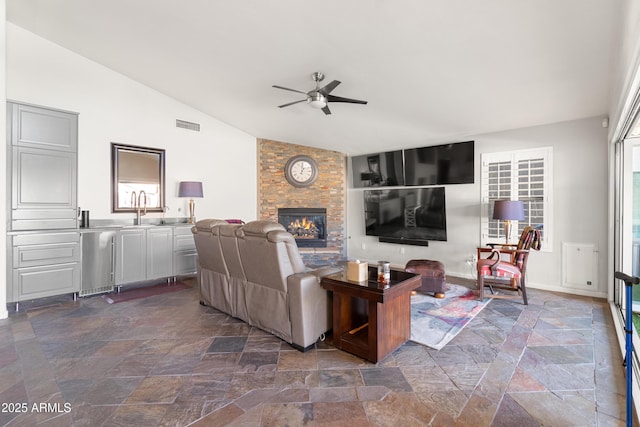 living room featuring a stone fireplace, ceiling fan, sink, and vaulted ceiling